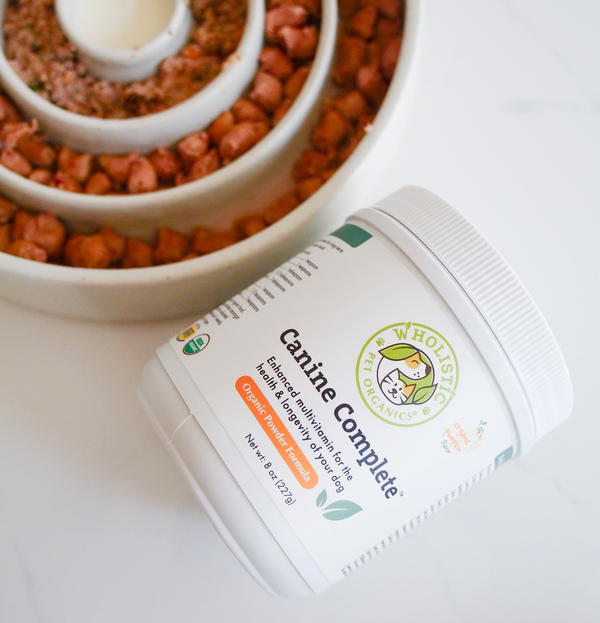 Dog bowl with kibble and Wholistic Pet Organics supplements, illustrating how whole-food supplements complete the diet.