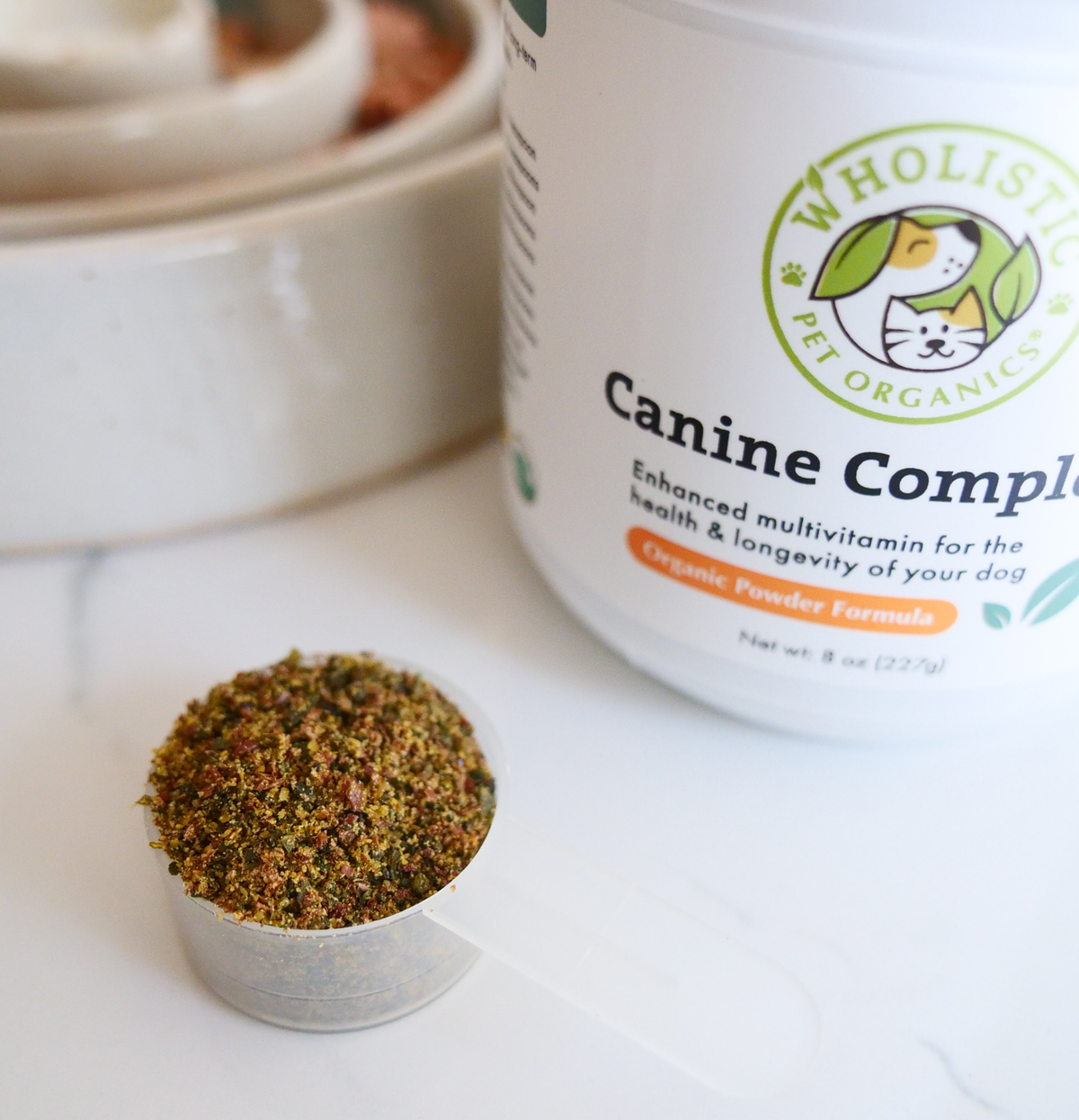 Dog bowl with kibble and Wholistic Pet Organics supplements, illustrating how whole-food supplements complete the diet.